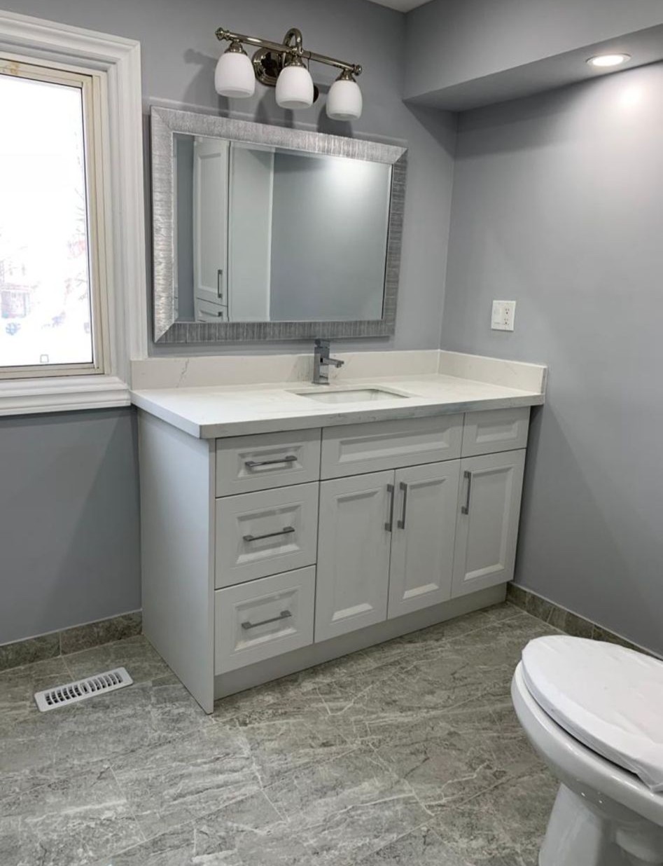 Modern bathroom vanity installation with white cabinetry and gray tile flooring in Toronto renovation